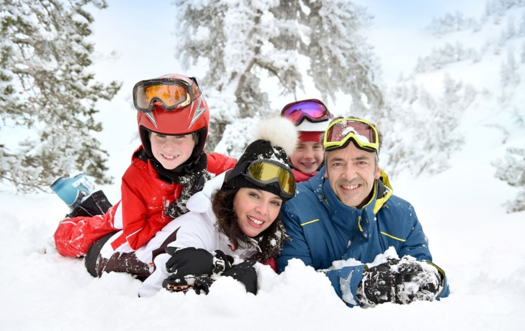 Mann Frau und Kinder liegen mit Schneeanzügen im Schnee