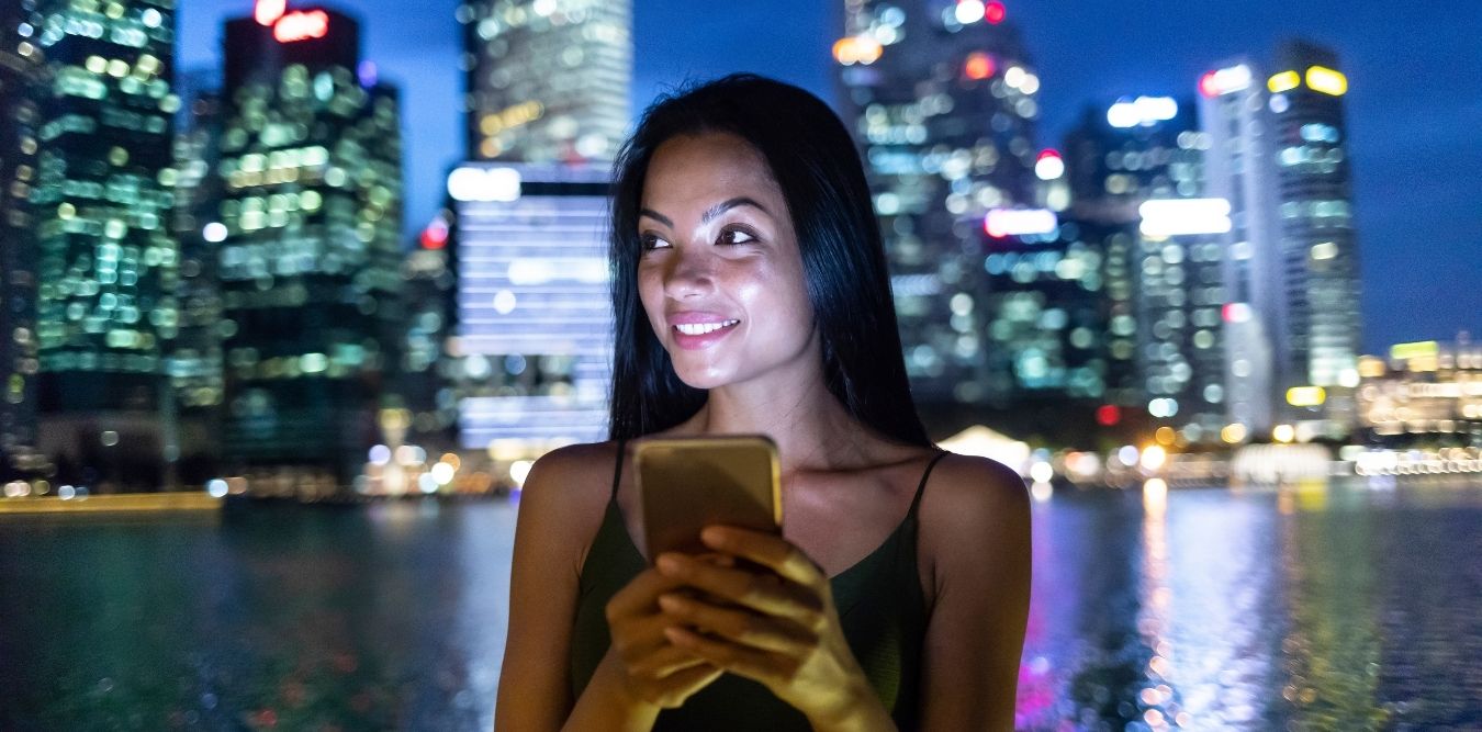 Frau in Singapur bei Nacht mit Smartphone