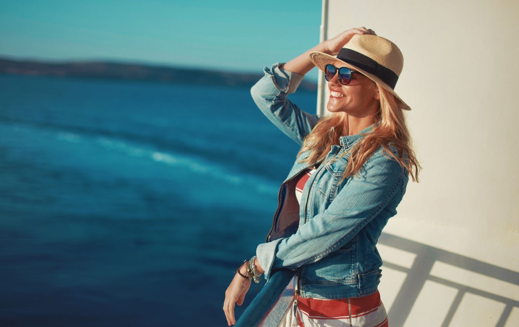 Frau mit Hut und Sonnenbrille schaut auf das Meer