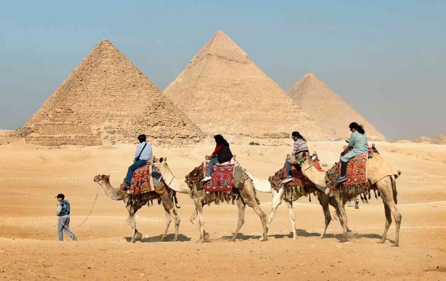 Touristen auf Kamelen vor den Pyramiden von Gizeh in Ägypten