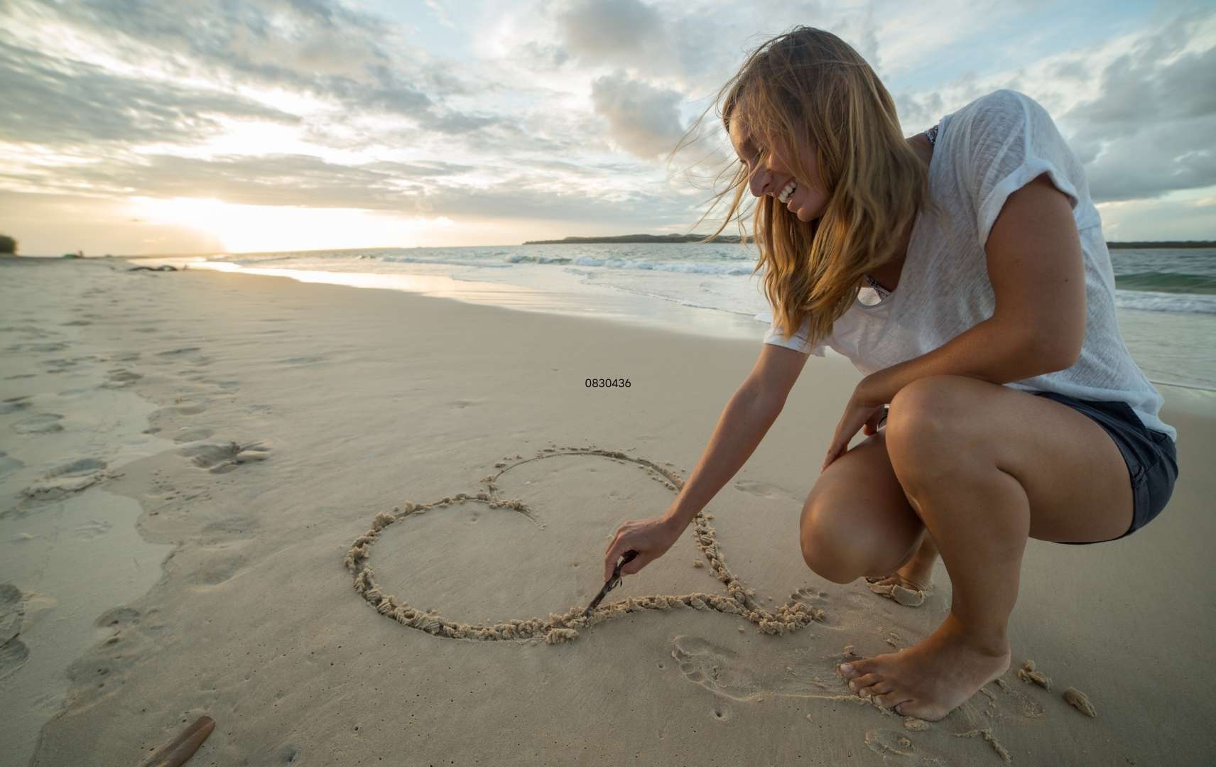 Frau malt Herz in Strand