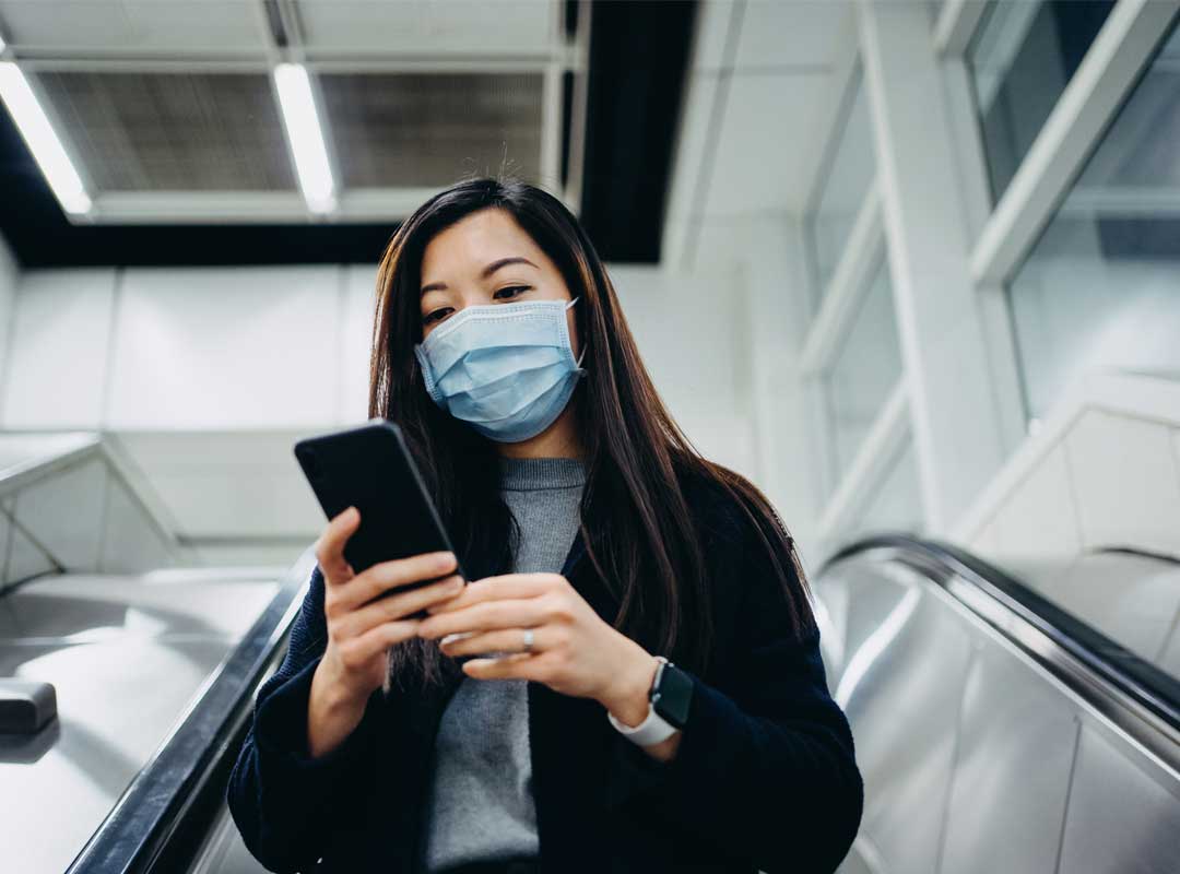 Junge asiatische Geschäftsfrau mit Smartphone und Maske auf Treppe