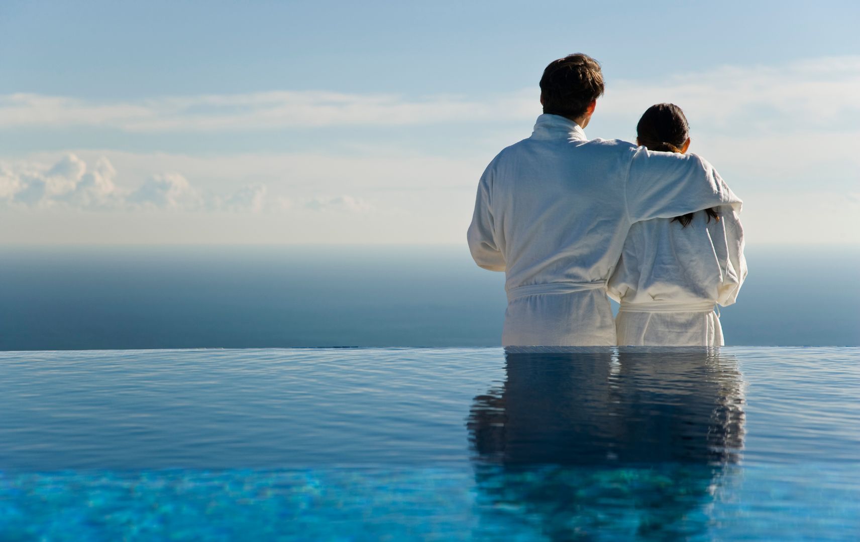 Paar im Bademantel blickt aufs Meer, davor Infinity Pool
