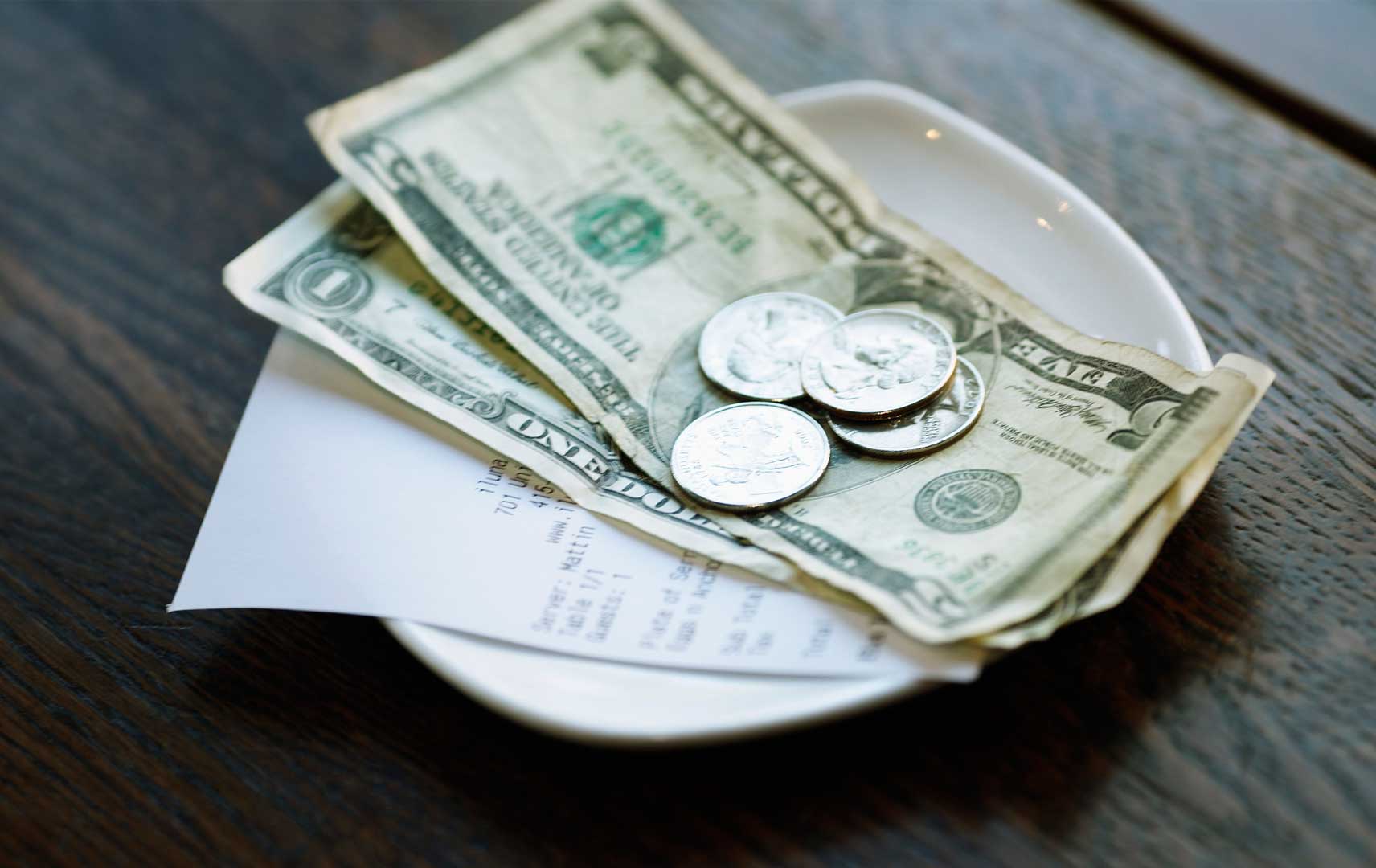 Dollarnoten und Münzen auf einem Teller mit einer Rechnung