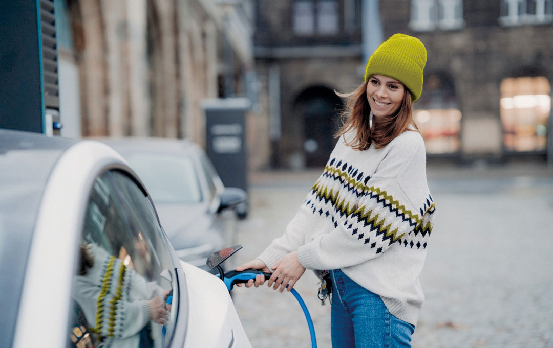 Junge lächelnde Frau mit Wollmütze lädt Elektroauto