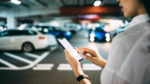 Frau blickt auf Smartphone in Tiefgarage mit Fahrzeugen im Hintergrund