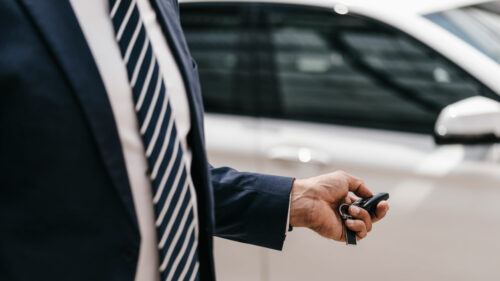 Geschäftsmann mit Autoschlüssel vor weißem Fahrzeug