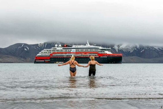 Zwei Frauen in Badeanzügen vor einem Schiff gehen ins Wasser