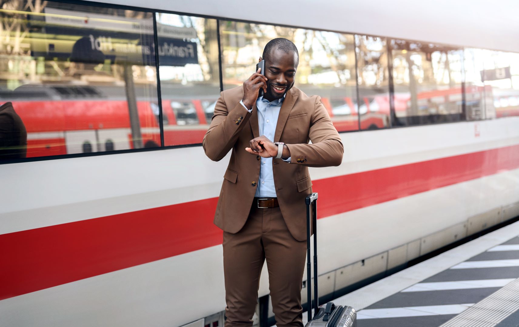 Deutsche Bahn - Geschäftsreisender mit Rollkoffer wartet am Bahnsteig am Zug, telefoniert und schaut auf die Uhr