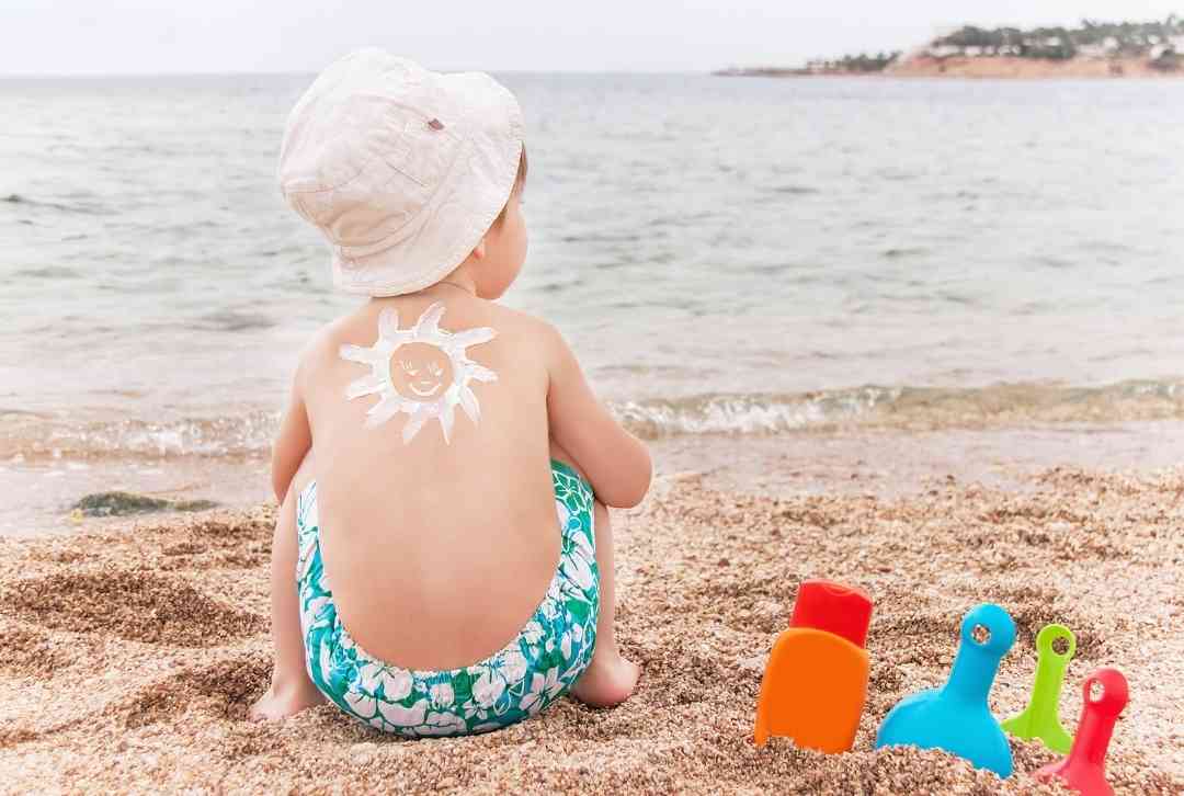 Baby sitzt am Strand mit einer Sonne aus Sonnencreme auf dem Rücken